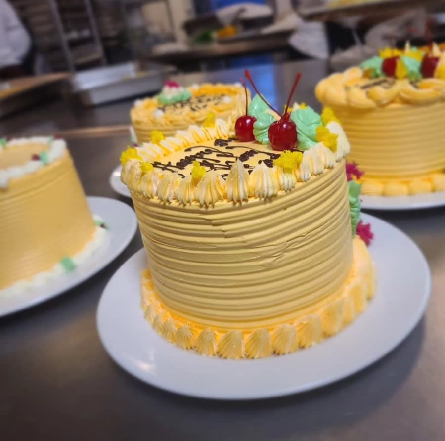 Tall yellow buttercream cakes with combed sides, cherries and piped flowers