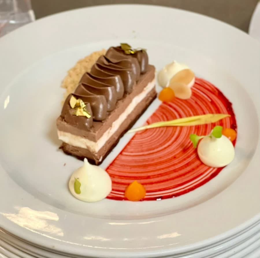 Plated chocolate mousse bar with gold leaf, meringue kisses and a red berry sauce swirl